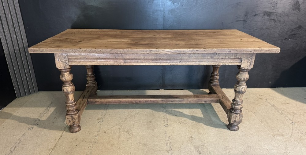 A solid oak farmhouse dining table with a thick plank top, turned baluster legs, and a low central stretcher rail. View VI