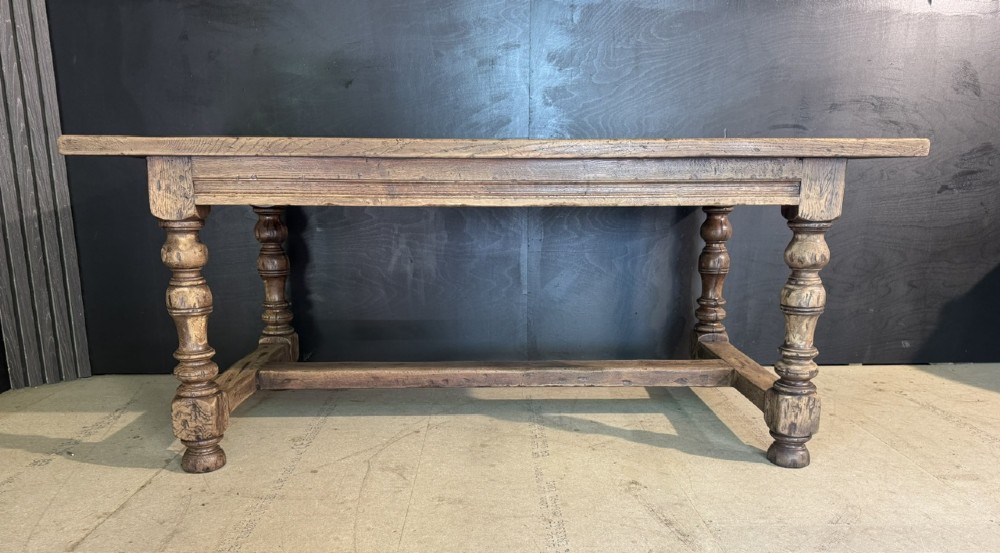 A solid oak farmhouse dining table with a thick plank top, turned baluster legs, and a low central stretcher rail. View VII