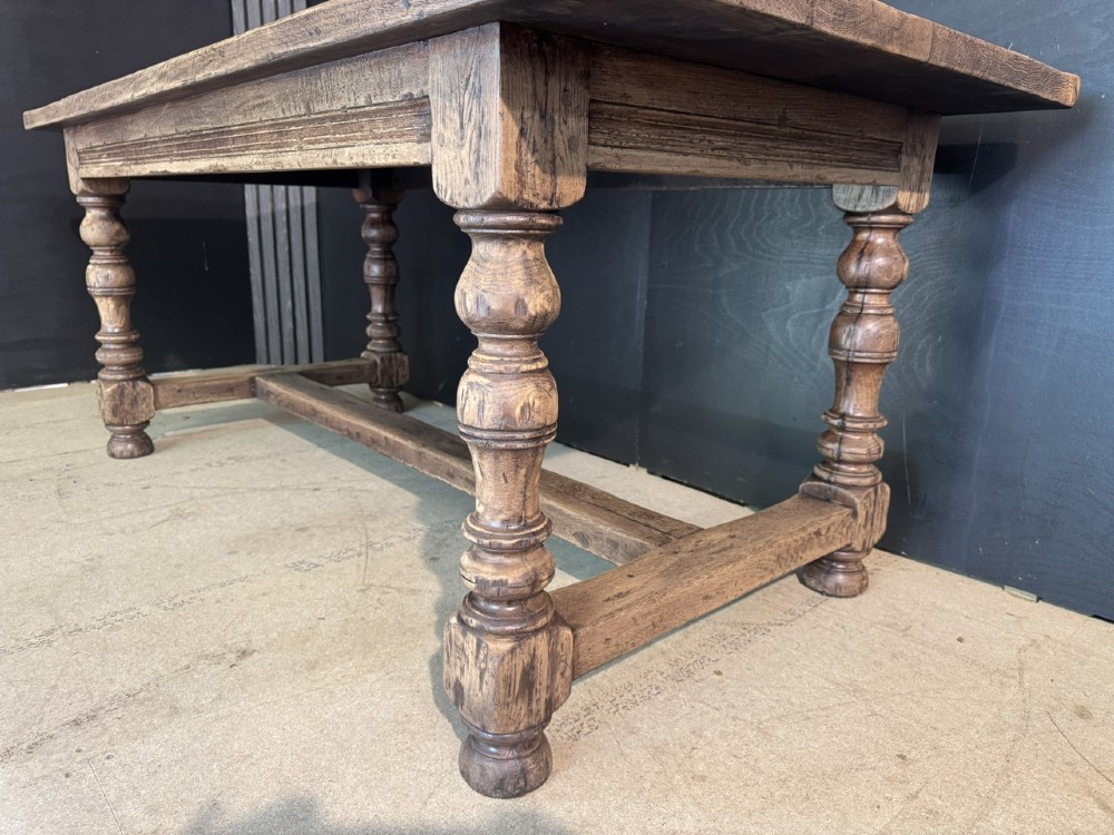 A solid oak farmhouse dining table with a thick plank top, turned baluster legs, and a low central stretcher rail. View X
