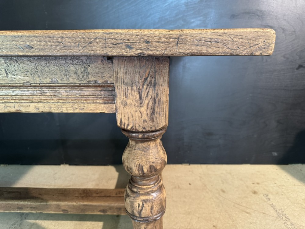 A solid oak farmhouse dining table with a thick plank top, turned baluster legs, and a low central stretcher rail. View XI
