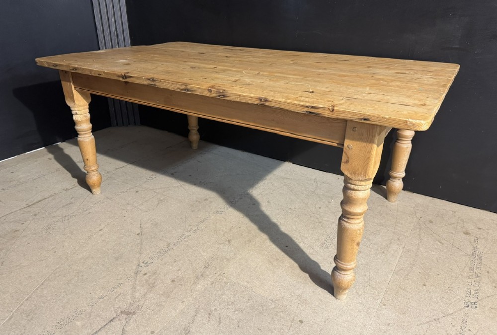 A rectangular pine farmhouse dining table featuring a solid plank top and four turned wooden legs.