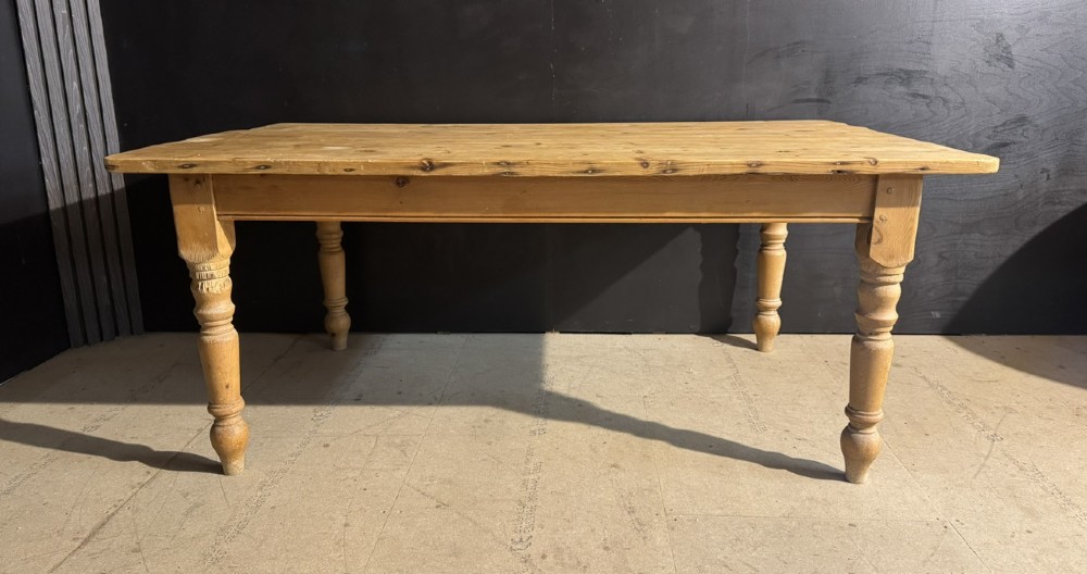A rectangular pine farmhouse dining table featuring a solid plank top and four turned wooden legs. View V