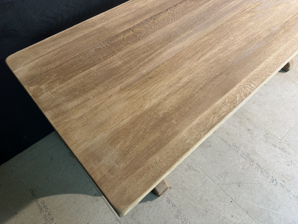 A long bleached oak dining table featuring a solid rectangular top supported by curved trestle legs connected by a central stretcher beam. View VIII