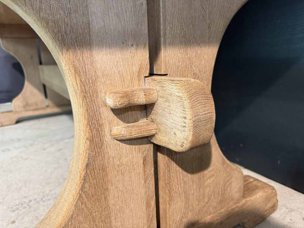 A long bleached oak dining table featuring a solid rectangular top supported by curved trestle legs connected by a central stretcher beam. View X