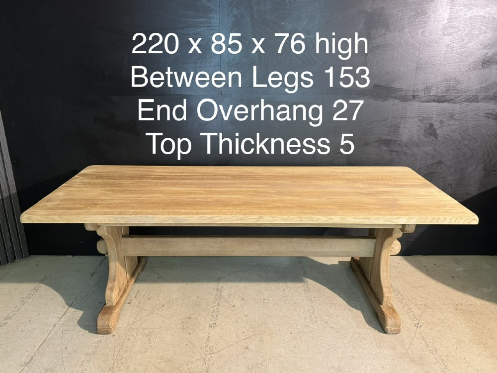 A long bleached oak dining table featuring a solid rectangular top supported by curved trestle legs connected by a central stretcher beam. View XIV