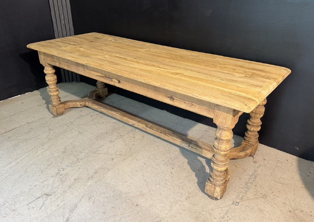 A long light oak French farmhouse table featuring a thick plank top, two frieze drawers, thick turned legs, and an H-stretcher base. View II