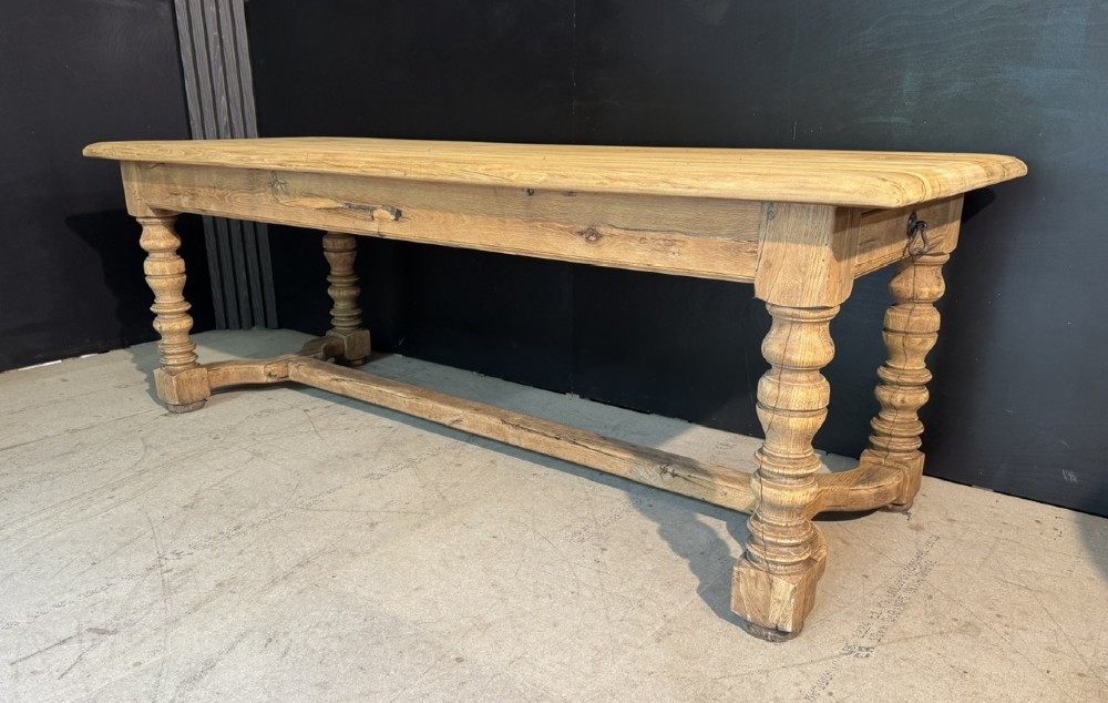 A long light oak French farmhouse table featuring a thick plank top, two frieze drawers, thick turned legs, and an H-stretcher base. View III