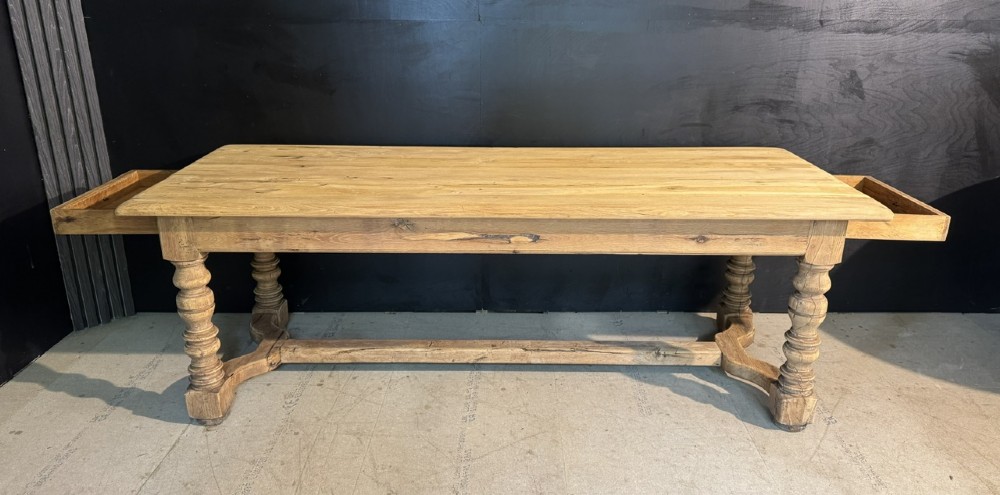 A long light oak French farmhouse table featuring a thick plank top, two frieze drawers, thick turned legs, and an H-stretcher base. View VII