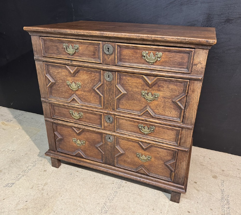 An eighteenth-century oak chest of drawers featuring geometric moulded drawer fronts, brass handles, and square block feet. View II