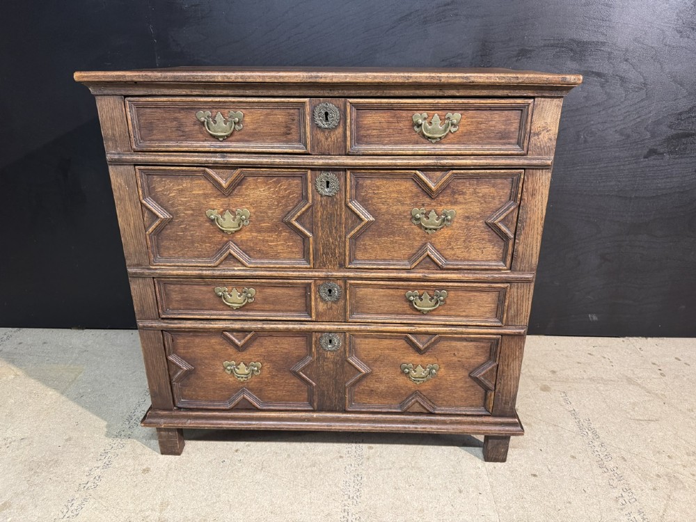 An eighteenth-century oak chest of drawers featuring geometric moulded drawer fronts, brass handles, and square block feet. View III
