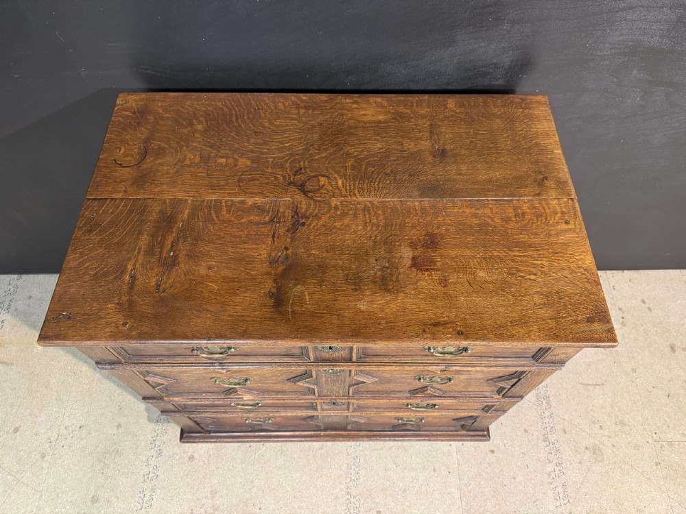 An eighteenth-century oak chest of drawers featuring geometric moulded drawer fronts, brass handles, and square block feet. View IV