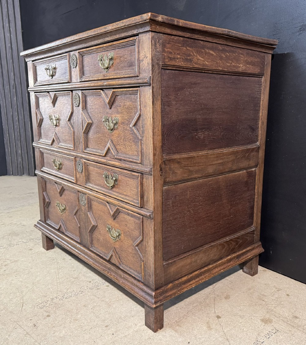 An eighteenth-century oak chest of drawers featuring geometric moulded drawer fronts, brass handles, and square block feet. View V