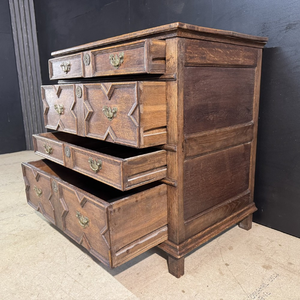 An eighteenth-century oak chest of drawers featuring geometric moulded drawer fronts, brass handles, and square block feet. View VI