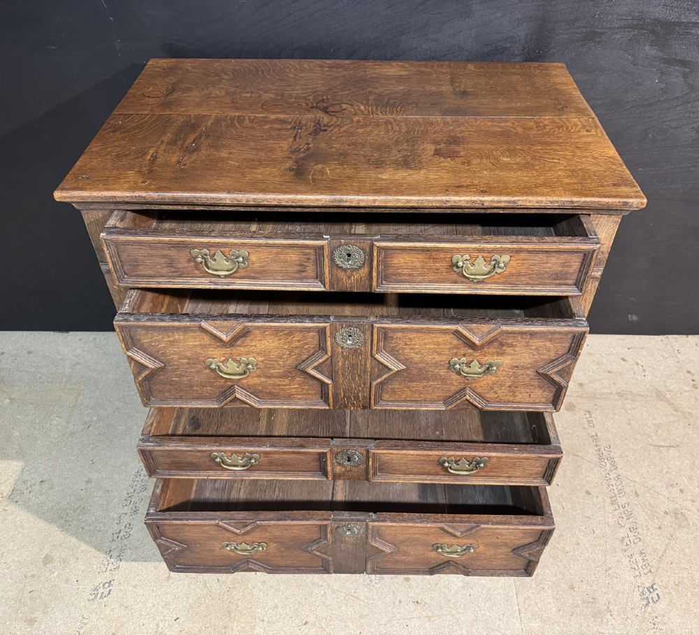 An eighteenth-century oak chest of drawers featuring geometric moulded drawer fronts, brass handles, and square block feet. View VII
