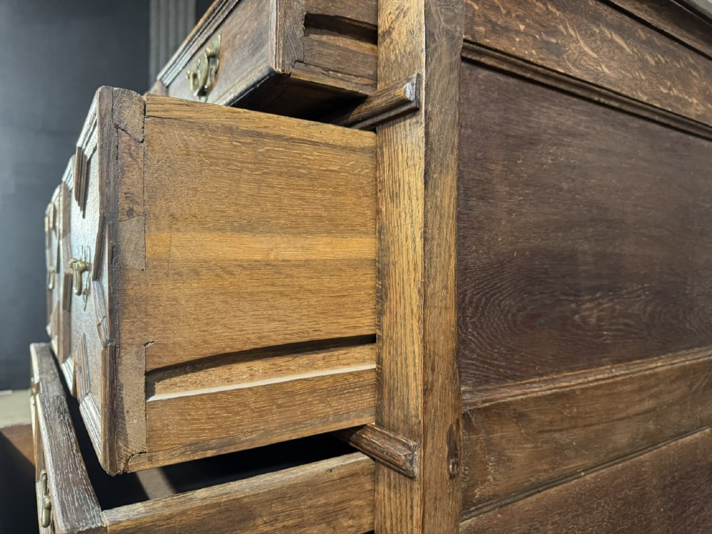 An eighteenth-century oak chest of drawers featuring geometric moulded drawer fronts, brass handles, and square block feet. View VIII