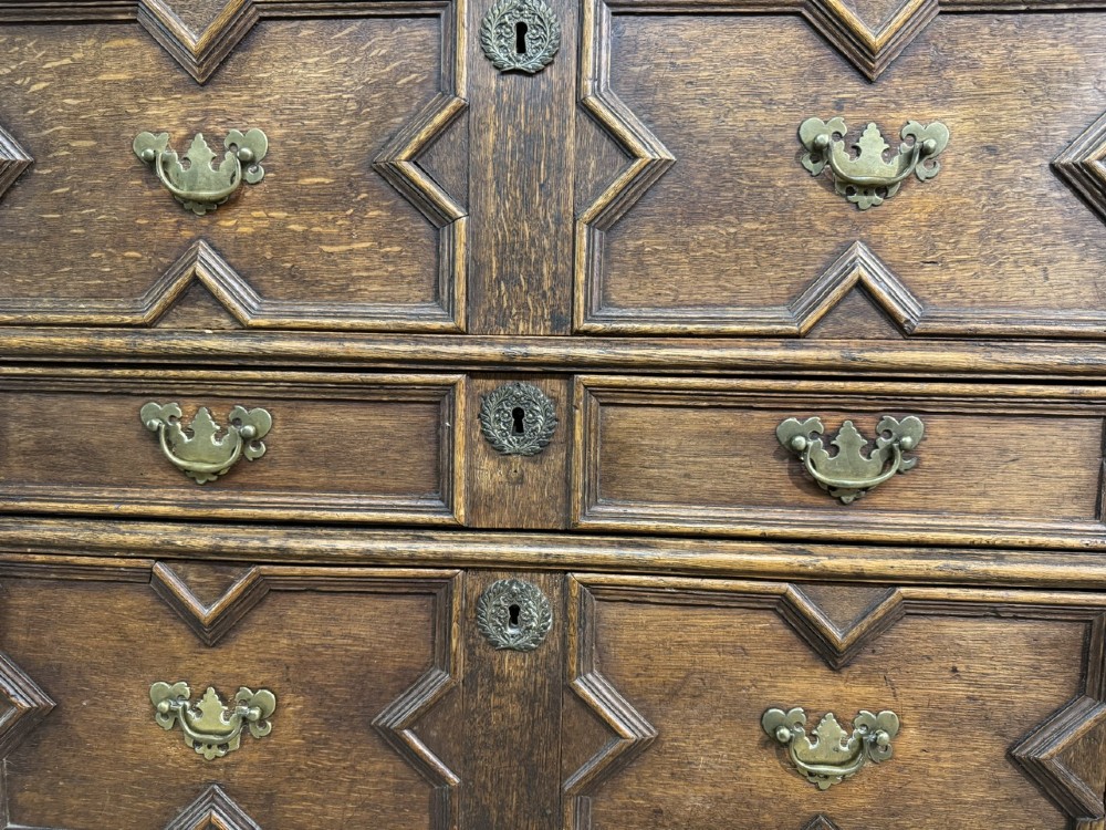 An eighteenth-century oak chest of drawers featuring geometric moulded drawer fronts, brass handles, and square block feet. View XIII