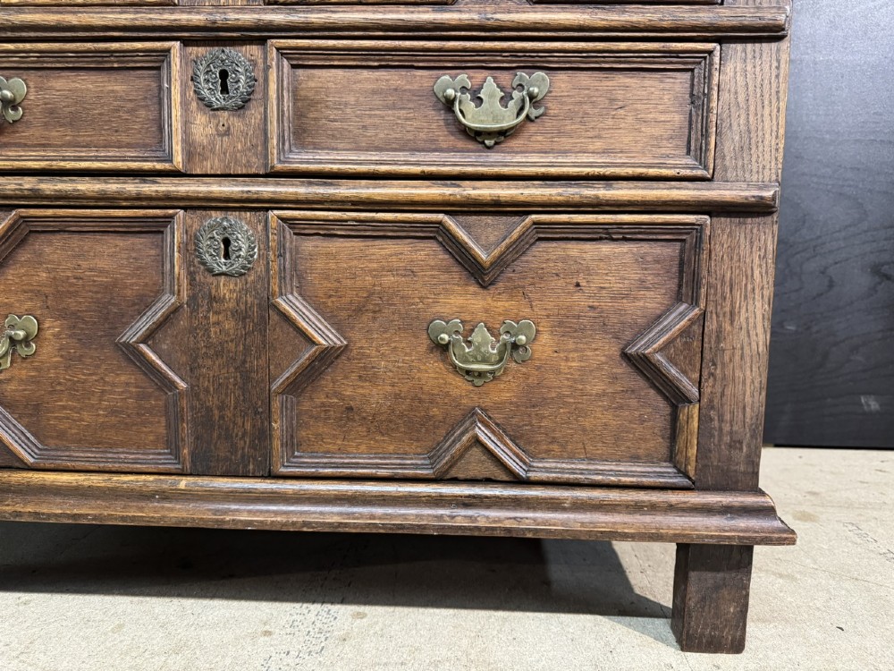 An eighteenth-century oak chest of drawers featuring geometric moulded drawer fronts, brass handles, and square block feet. View XIV