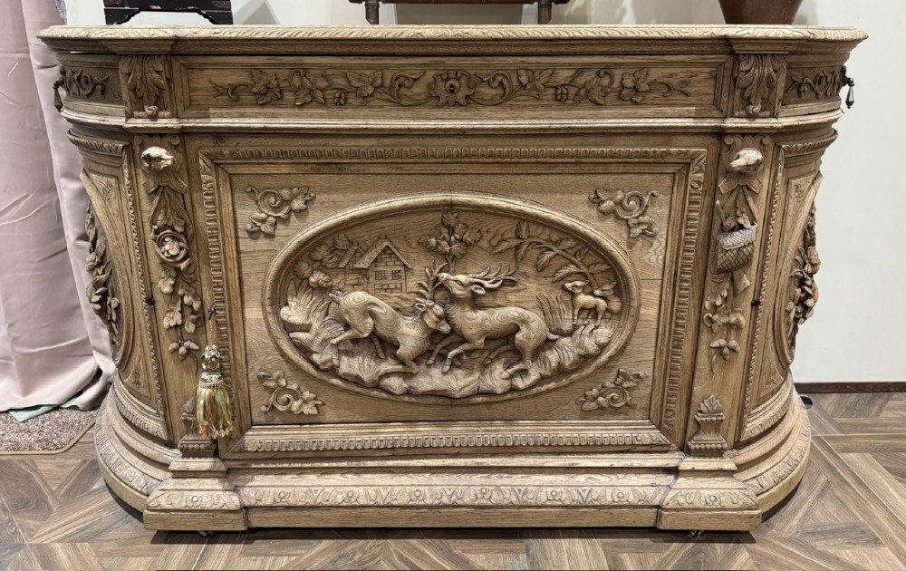 A light oak sideboard with detailed relief carvings of deer in a forest setting on the central panel, flanked by foliage motifs.