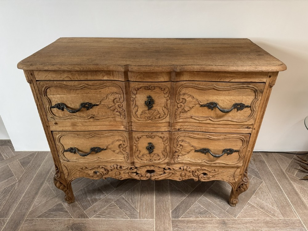 A French bleached oak two-drawer commode featuring carved foliate panels, cabriole legs, and dark metal handles. View II