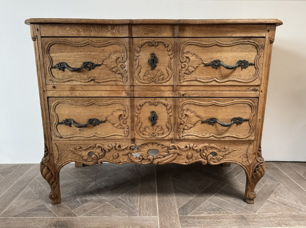 A French bleached oak two-drawer commode featuring carved foliate panels, cabriole legs, and dark metal handles. View IV