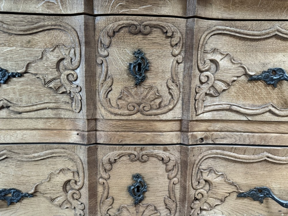 A French bleached oak two-drawer commode featuring carved foliate panels, cabriole legs, and dark metal handles. View V