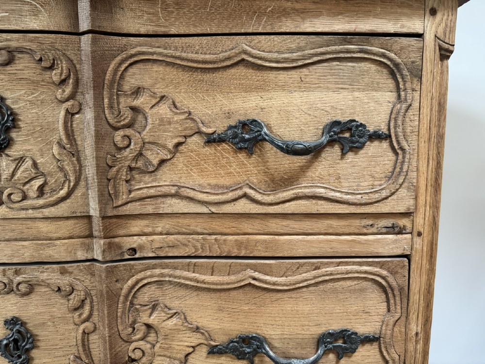 A French bleached oak two-drawer commode featuring carved foliate panels, cabriole legs, and dark metal handles. View VI