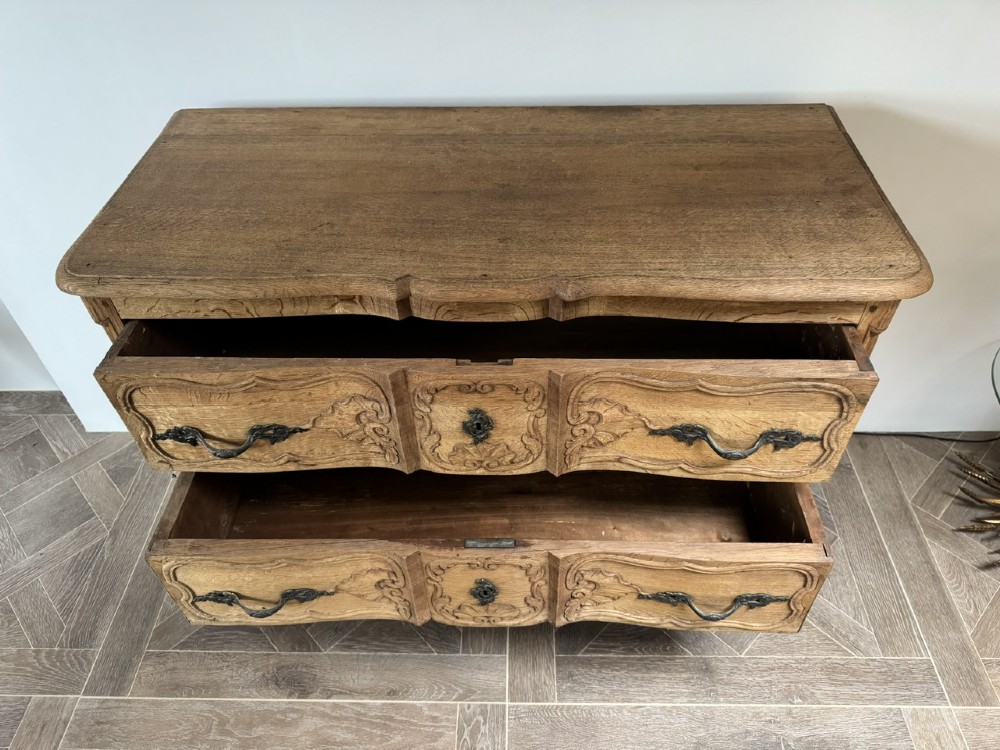 A French bleached oak two-drawer commode featuring carved foliate panels, cabriole legs, and dark metal handles. View IX