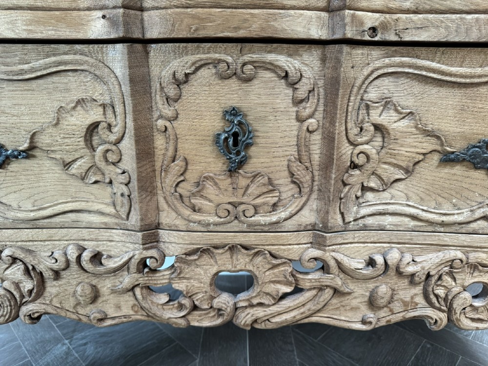 A French bleached oak two-drawer commode featuring carved foliate panels, cabriole legs, and dark metal handles. View XI