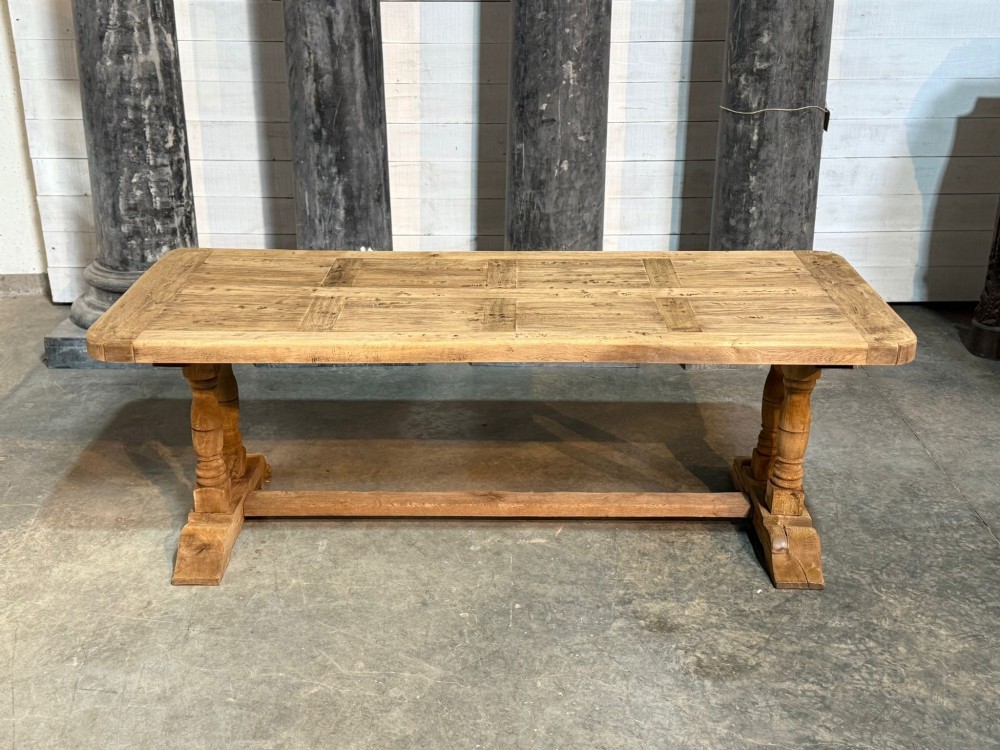 A rectangular French oak dining table featuring a parquetry top, twin turned pedestal legs, and a low central stretcher base.