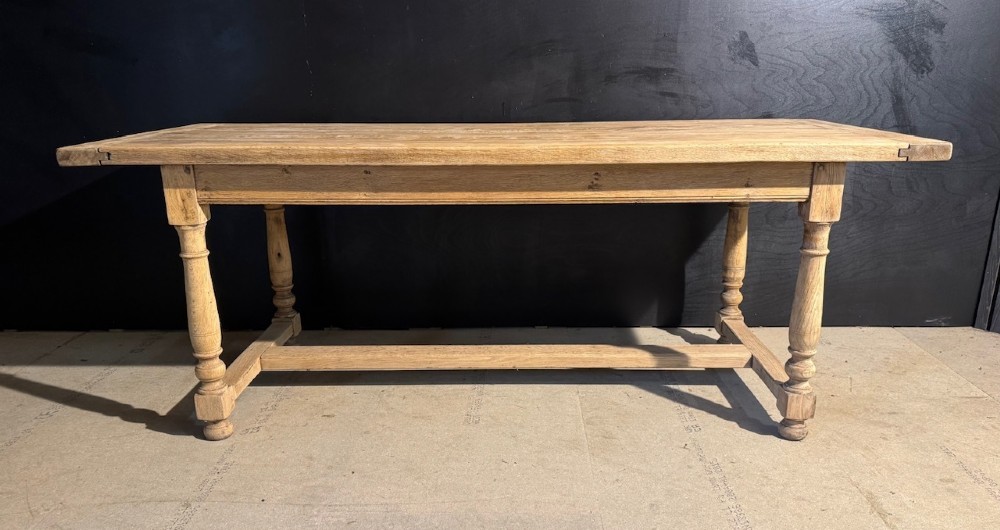 A light natural oak farmhouse dining table featuring turned legs, an H-stretcher base, and a planked top with cleated breadboard ends.