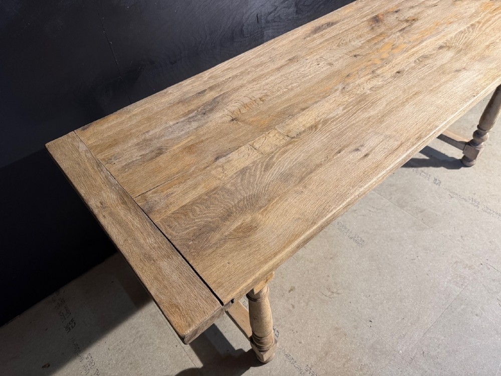 A light natural oak farmhouse dining table featuring turned legs, an H-stretcher base, and a planked top with cleated breadboard ends. View VI