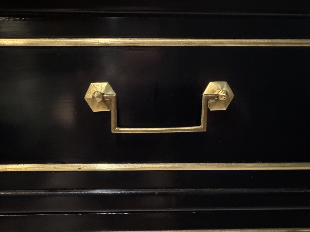 An ebonised Louis XVI style chest of drawers featuring three long drawers with brass rectangular mouldings, geometric handles, fluted tapered legs, and a white marble top. View XI