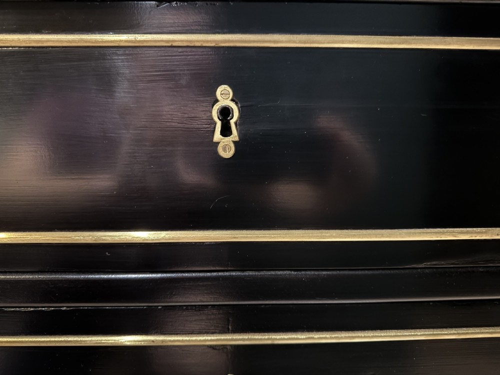 An ebonised Louis XVI style chest of drawers featuring three long drawers with brass rectangular mouldings, geometric handles, fluted tapered legs, and a white marble top. View XII