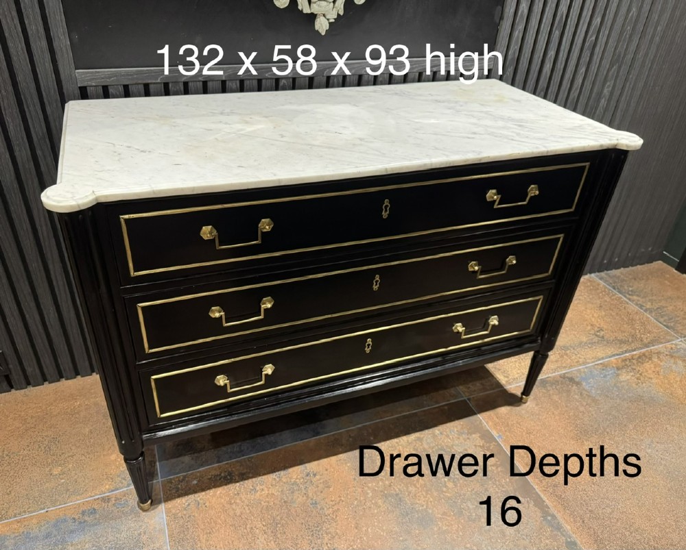 An ebonised Louis XVI style chest of drawers featuring three long drawers with brass rectangular mouldings, geometric handles, fluted tapered legs, and a white marble top. View XV