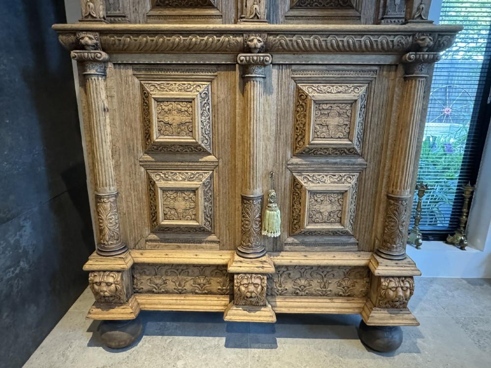 An 18th-century Flemish carved oak cabinet featuring detailed figurative columns, geometric door panels, lion head motifs, and bun feet. View III