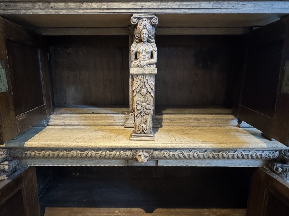 An 18th-century Flemish carved oak cabinet featuring detailed figurative columns, geometric door panels, lion head motifs, and bun feet. View IX