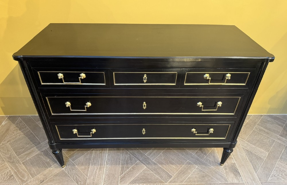 A French Louis XVI style ebonised commode featuring three tiers of drawers detailed with geometric brass trim and supported by tapered fluted legs. View II