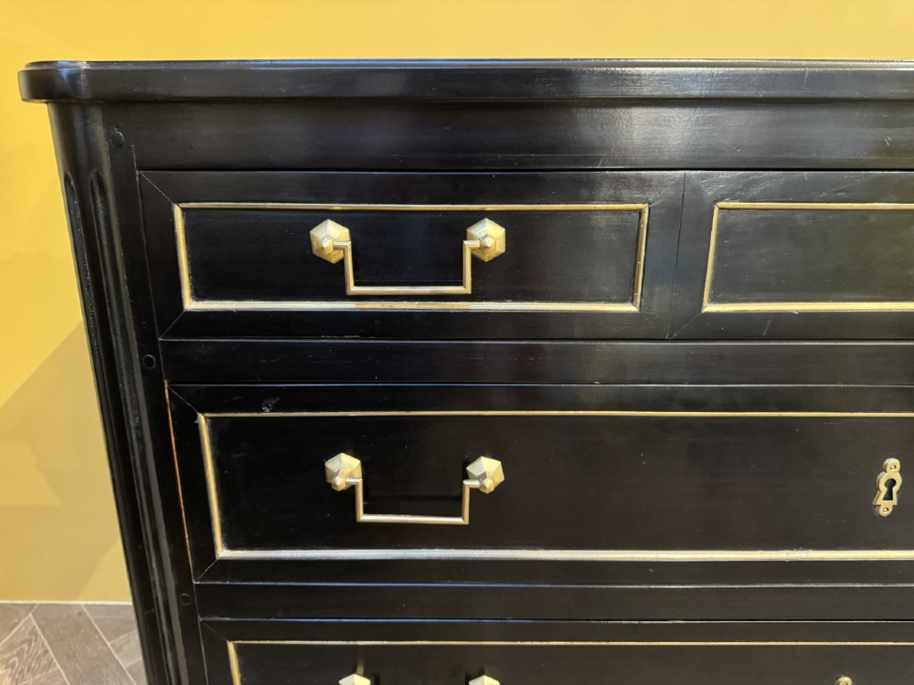 A French Louis XVI style ebonised commode featuring three tiers of drawers detailed with geometric brass trim and supported by tapered fluted legs. View V