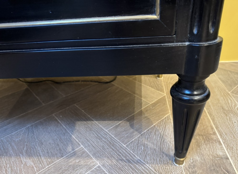 A French Louis XVI style ebonised commode featuring three tiers of drawers detailed with geometric brass trim and supported by tapered fluted legs. View VI