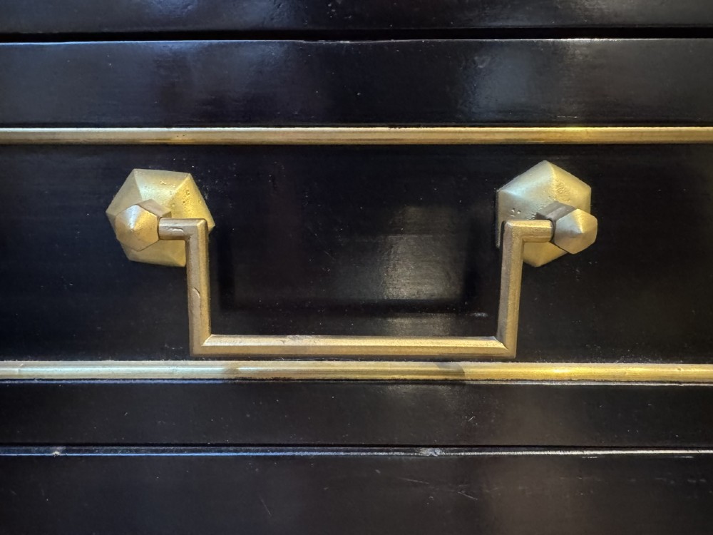 A French Louis XVI style ebonised commode featuring three tiers of drawers detailed with geometric brass trim and supported by tapered fluted legs. View VII