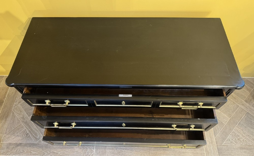 A French Louis XVI style ebonised commode featuring three tiers of drawers detailed with geometric brass trim and supported by tapered fluted legs. View VIII