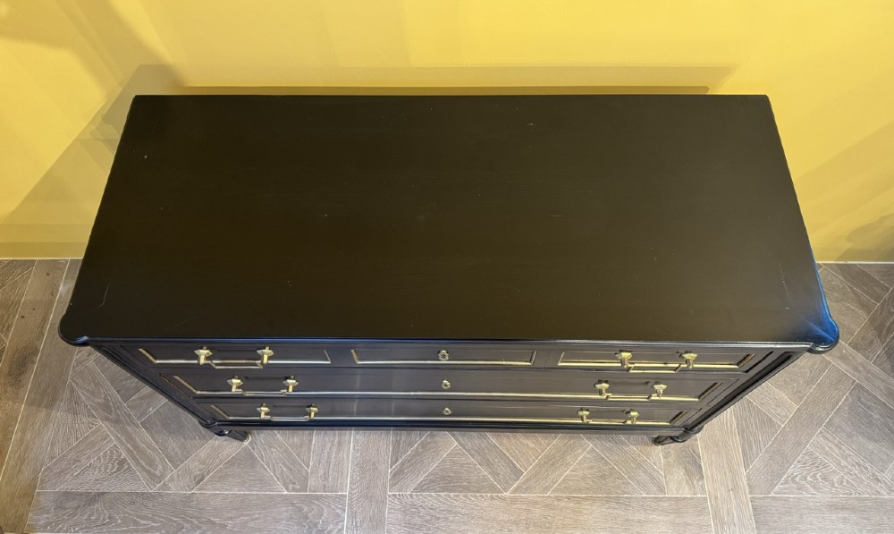 A French Louis XVI style ebonised commode featuring three tiers of drawers detailed with geometric brass trim and supported by tapered fluted legs. View XI
