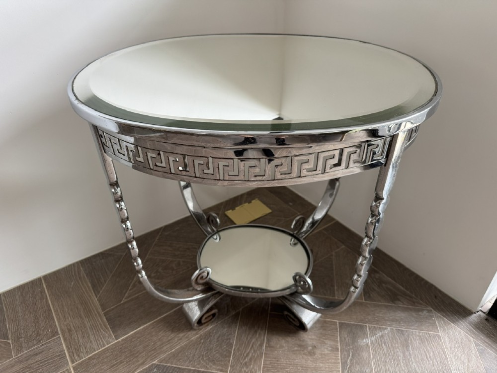 A circular chrome Art Deco side table featuring a mirrored glass top, Greek key frieze pattern, lower tier mirror, and scroll-footed legs.