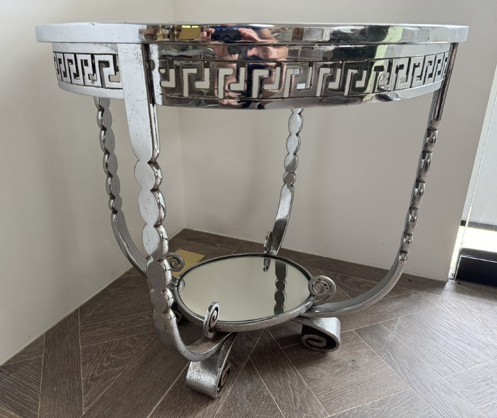 A circular chrome Art Deco side table featuring a mirrored glass top, Greek key frieze pattern, lower tier mirror, and scroll-footed legs. View VII
