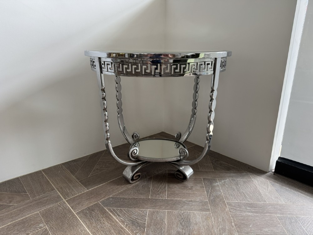 A circular chrome Art Deco side table featuring a mirrored glass top, Greek key frieze pattern, lower tier mirror, and scroll-footed legs. View IX