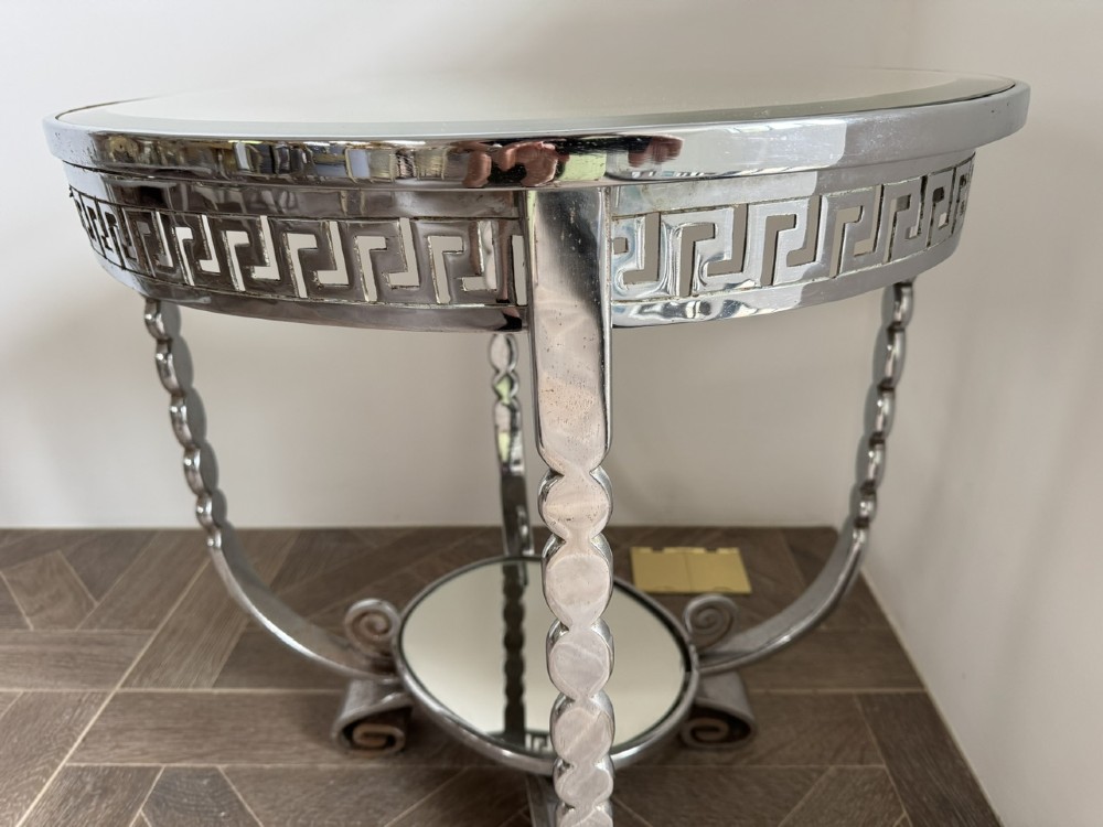 A circular chrome Art Deco side table featuring a mirrored glass top, Greek key frieze pattern, lower tier mirror, and scroll-footed legs. View X