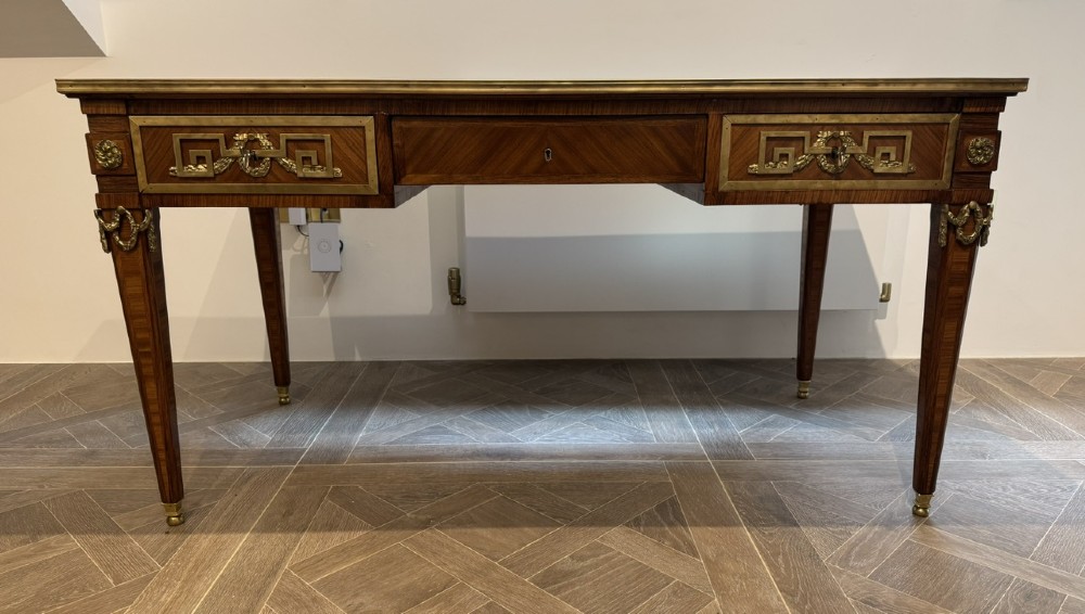 A French Louis XVI style writing desk featuring a green leather insert, wood parquetry veneer, three frieze drawers, and gilt bronze mounts. View II