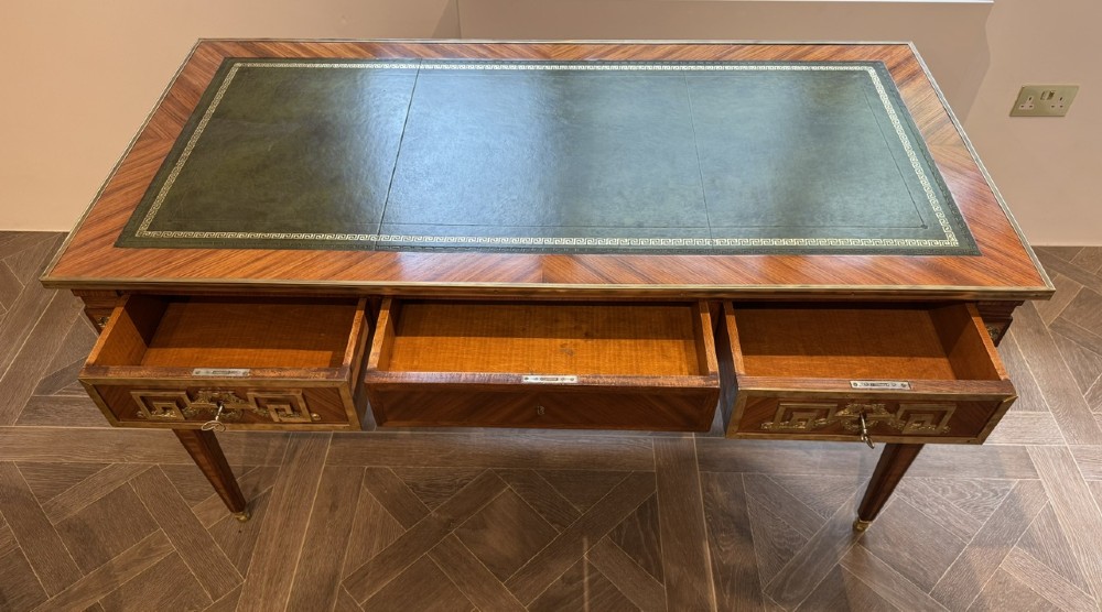 A French Louis XVI style writing desk featuring a green leather insert, wood parquetry veneer, three frieze drawers, and gilt bronze mounts. View IV