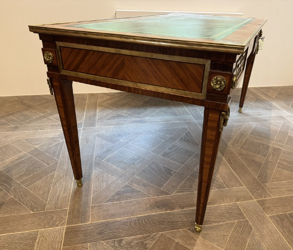 A French Louis XVI style writing desk featuring a green leather insert, wood parquetry veneer, three frieze drawers, and gilt bronze mounts. View X