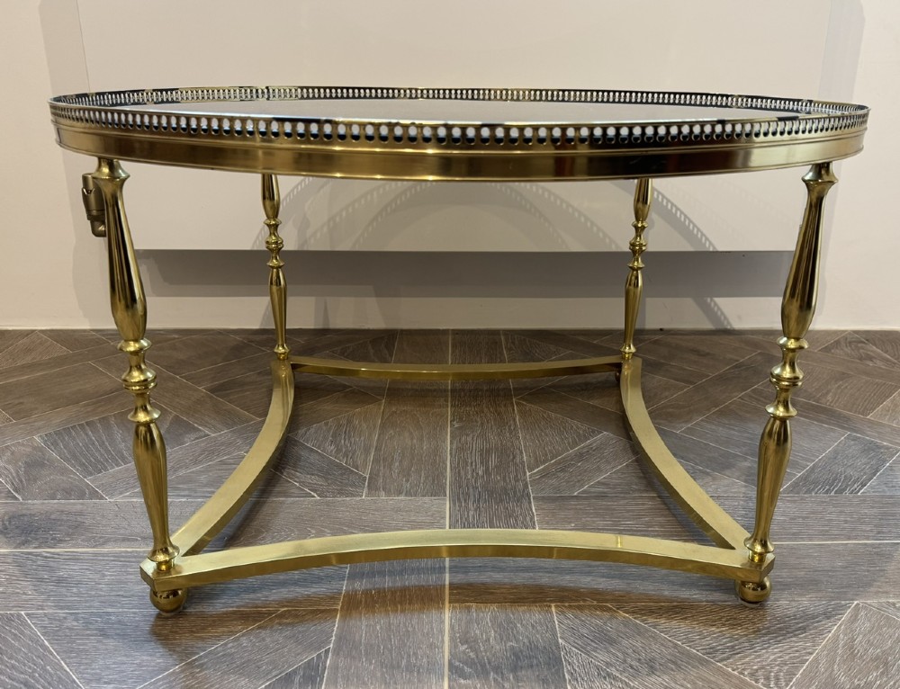 A circular brass coffee table featuring a dark smoked glass top, a pierced gallery rim, turned legs, and a curved stretcher base. View II